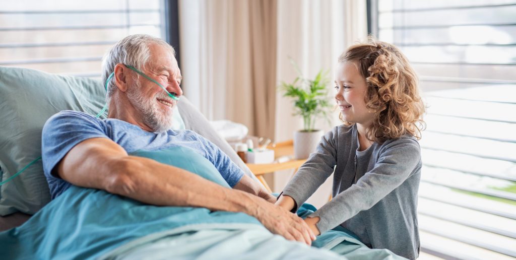 Man in hospital bed holding hands with young girl