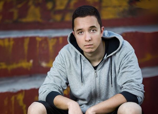 A teen wearing a grey hoodie stitting on steps