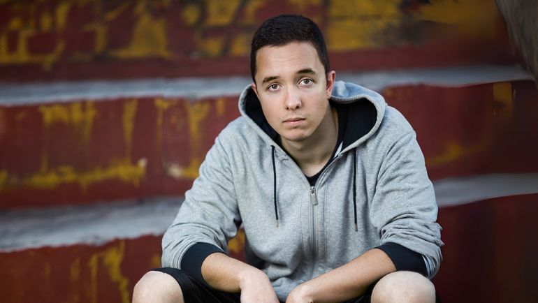 A teen wearing a grey hoodie stitting on steps