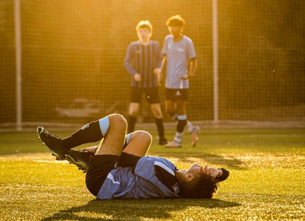 Soccer Player on the Ground with Two Players Looking on