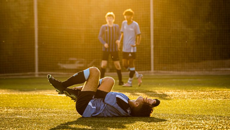 Soccer Player on the Ground with Two Players Looking on